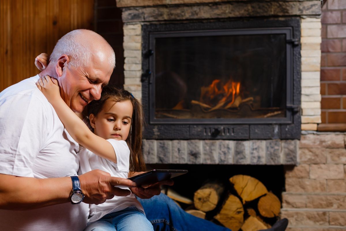 Grandfather and granddaughter using tablet of a house near the fireplace